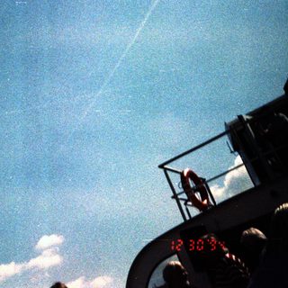 Person on ship observing daytime sky with visible contrails.