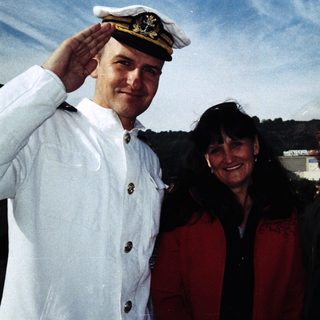 Three people posing together outdoors in naval and casual attire.