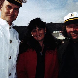 Three people posing together outdoors in naval and casual attire.