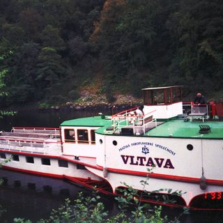 Steamship "Vltava" on river with lush surroundings.