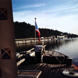 Boat docked near Prague river with Czech flag.