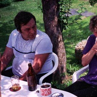 Two people outdoors enjoying drinks and conversation with a dog.