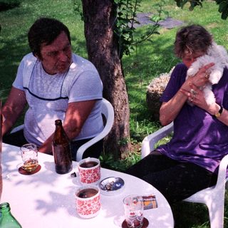 Two people outdoors enjoying drinks and conversation with a dog.