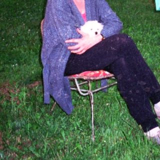 Two people sitting outdoors on chairs, holding a small white object.