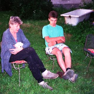 Two people sitting outdoors on chairs, holding a small white object.