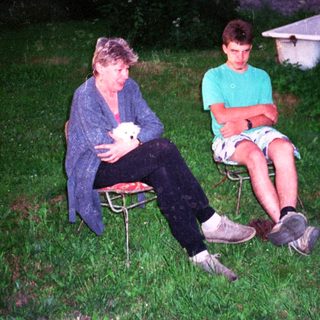 Two people sitting outdoors on chairs, holding a small white object.