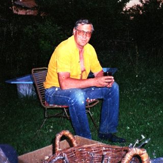 Man sitting outdoors at dusk holding drink.