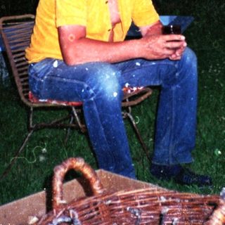 Man sitting outdoors at dusk holding drink.