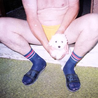 Person kneeling holds small white puppy indoors.