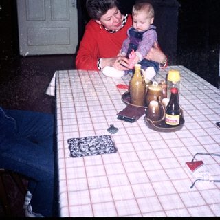 Woman holding baby at kitchen table with bottles.