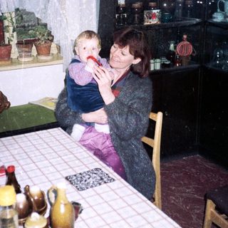 Woman holding child in vintage kitchen setting.