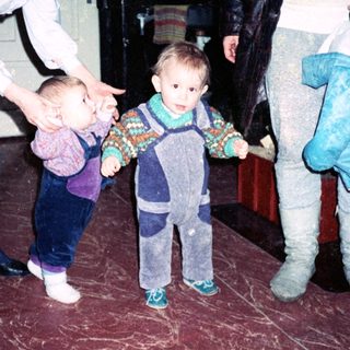 Two adults assist toddlers learning to walk indoors.