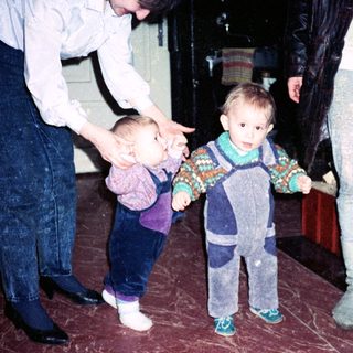 Two adults assist toddlers learning to walk indoors.
