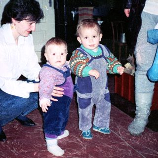 Family indoor moment with woman holding toddler, another child standing.