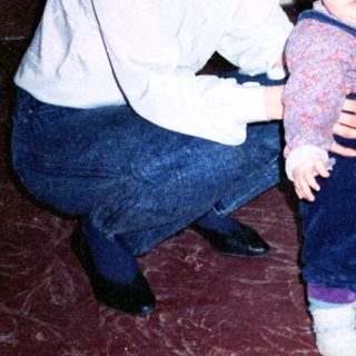 Family indoor moment with woman holding toddler, another child standing.