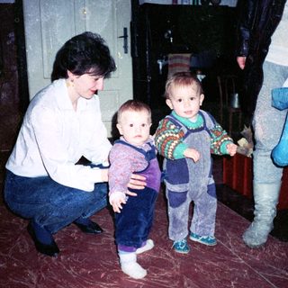 Family indoor moment with woman holding toddler, another child standing.