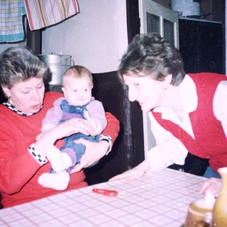 Two women holding and caring for a baby indoors.