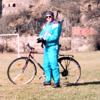 Person in cycling gear poses with bike near medieval ruins.