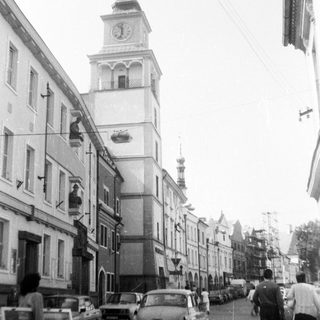 Historic European street with clock tower and vintage cars.