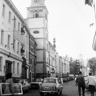 Historic European street with clock tower and vintage cars.