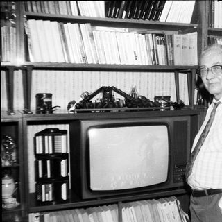 Old man posing with vintage TV and bookshelf.