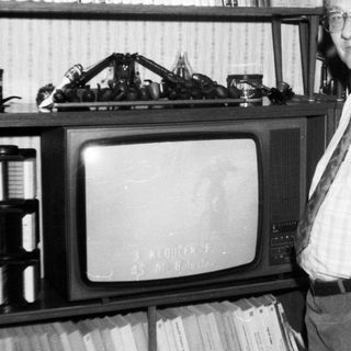Old man posing with vintage TV and bookshelf.