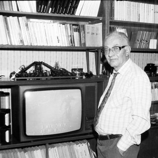 Old man posing with vintage TV and bookshelf.