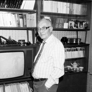 Old man posing with vintage TV and bookshelf.