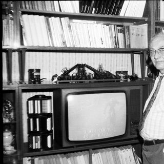 Old man posing with vintage TV and bookshelf.