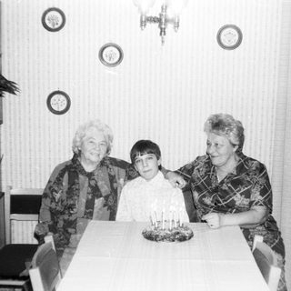 Three generations posing with birthday cake indoors.