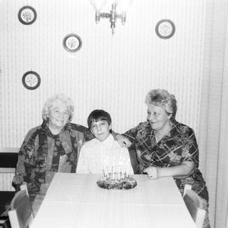 Three generations posing with birthday cake indoors.
