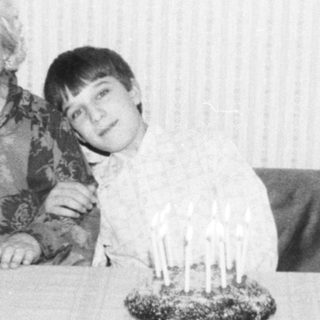 A woman and young boy posing indoors near a birthday cake.