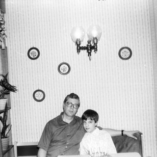 Two men posing indoors in vintage-style home setting.
