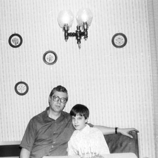 Two men posing indoors in vintage-style home setting.