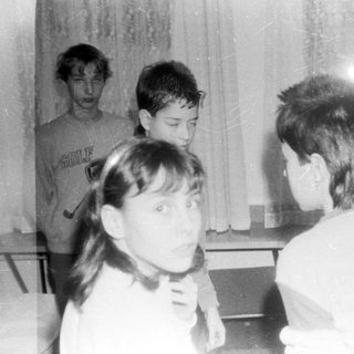Four children gathered indoors, focused on a screen.