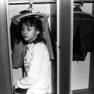 Person standing in narrow closet wearing hooded sweatshirt.