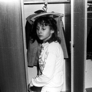 Person standing in narrow closet wearing hooded sweatshirt.