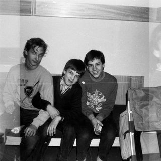 Four young men posing indoors in 1980s-style sweatshirts.