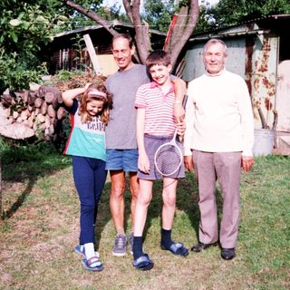 Family posing outdoors near rustic cabin with tennis racket.