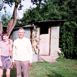 Family posing outdoors near rustic cabin with tennis racket.