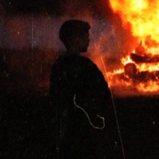 Large bonfire burning under rainy night sky.