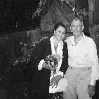 Couple visiting grave with floral tribute.