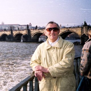 Man posing by Prague Castle with Charles Bridge and Vltava River.