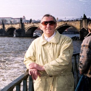 Man posing by Prague Castle with Charles Bridge and Vltava River.