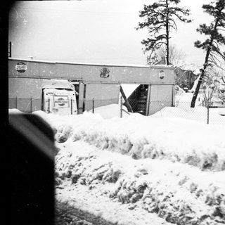 Snow-covered landscape with damaged buildings and heavy snow accumulation.