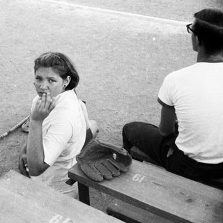 Woman sitting on dugout bench during baseball game.