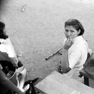 Woman sitting on dugout bench during baseball game.