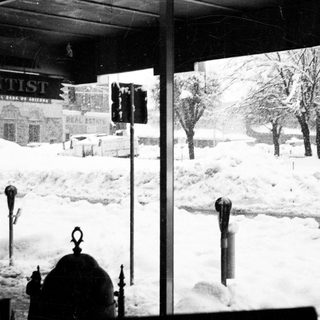 Snow-covered city street with visible signs for dentist and real estate.