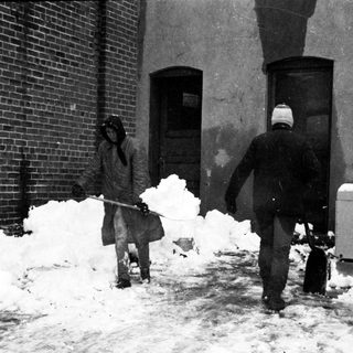 People shoveling heavy snow outside a building.