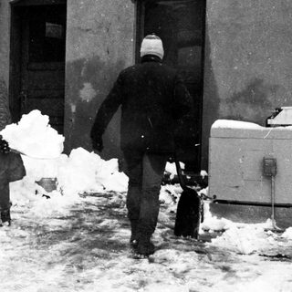 People shoveling heavy snow outside a building.